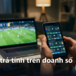 Điện thoại hiển thị danh sách trận bóng và tỷ lệ cược, laptop phía sau phát trận đấu trực tiếp